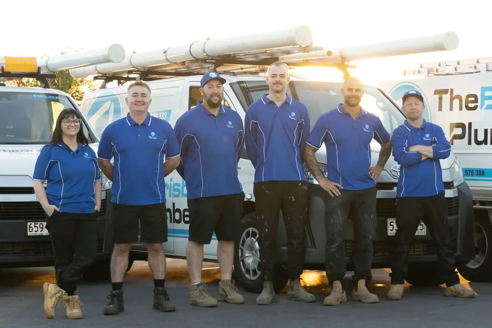 The Brisbane Plumbers team in uniform standing in front of their branded work vans
